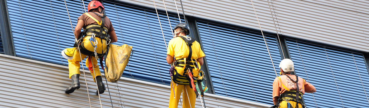 Fassadenreiniger in Berlin reinigen die Lamellen von Jalousien an einer Glasfassade