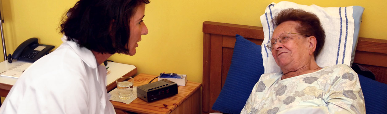 Seniorenpflege in Berlin: Ärztin spricht mit einer alten Frau im Bett